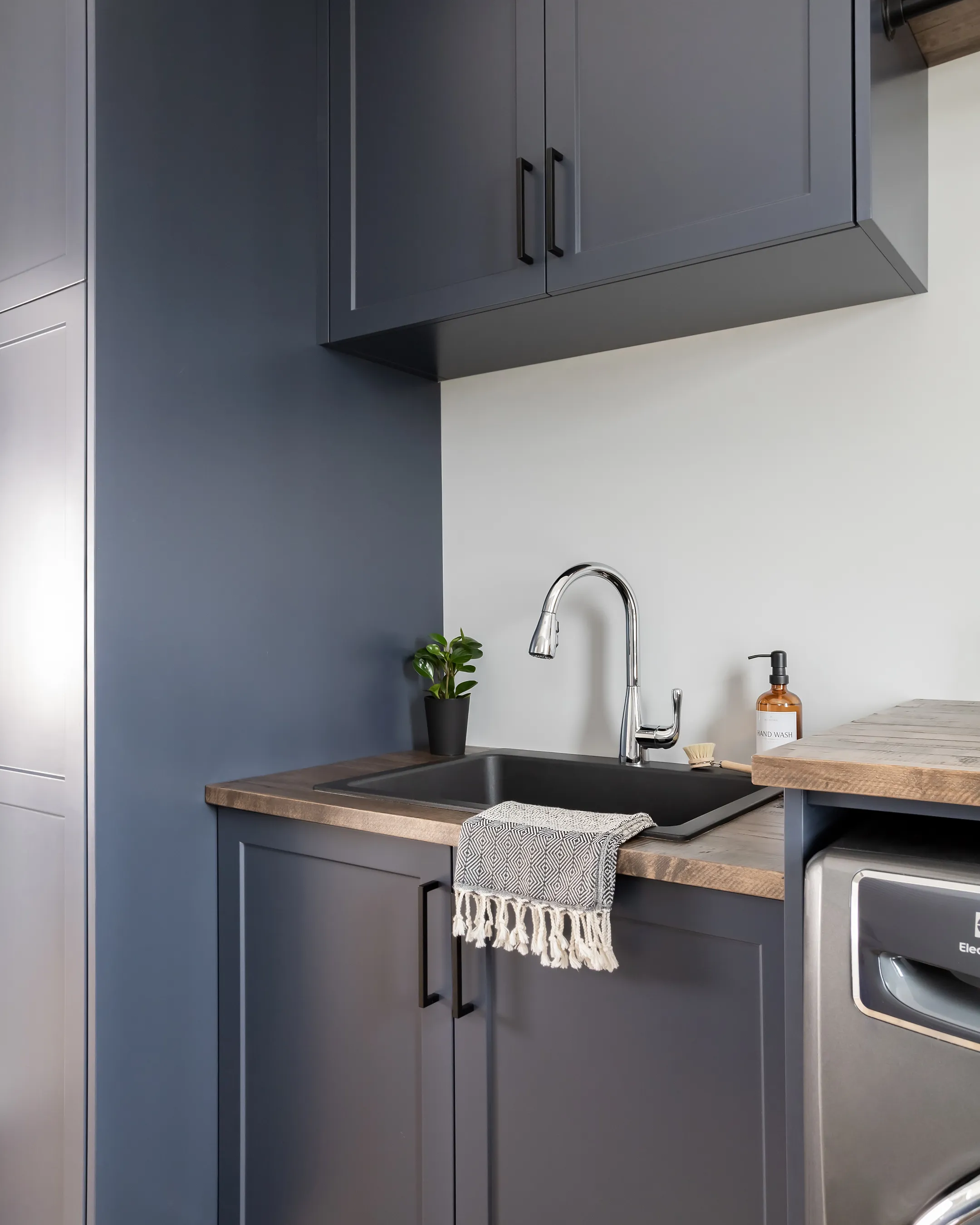 Custom charcoal laundry room cabinetry with wood countertop by Heirlooms